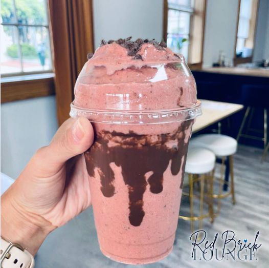 a hand holding a pink drink with chocolate drizzle in a clear to go cup